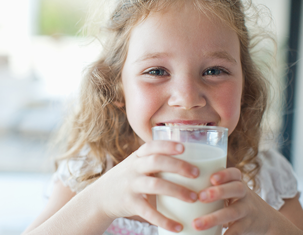 Little girl drinking a glass of milk while smiling - lactose intolerance