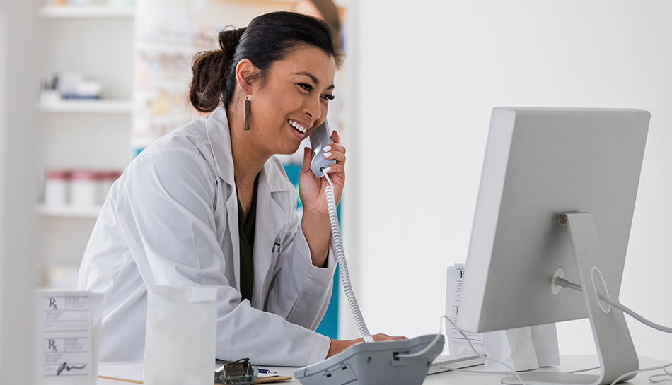 Pharmacist on computer and on phone talking to patient