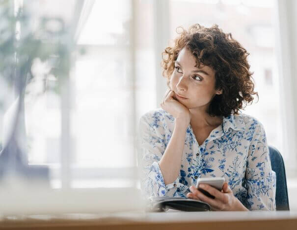 Pensive young woman holding her phone